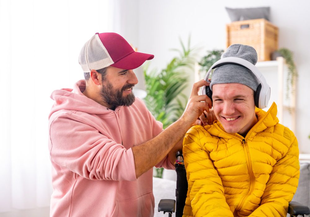 Caregiver helps young man with a disability and his adjust his headphones