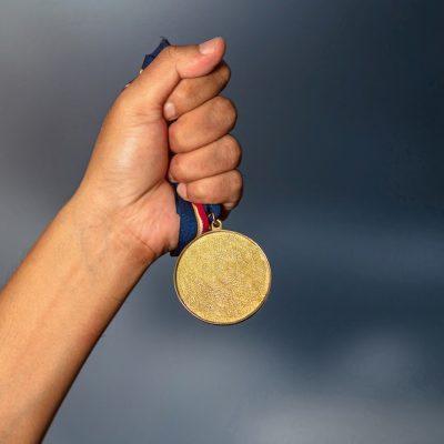 Hand holding gold medal on against cloudy sky background