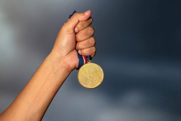 Hand holding gold medal on against cloudy sky background Hand holding gold medal on against cloudy sky background