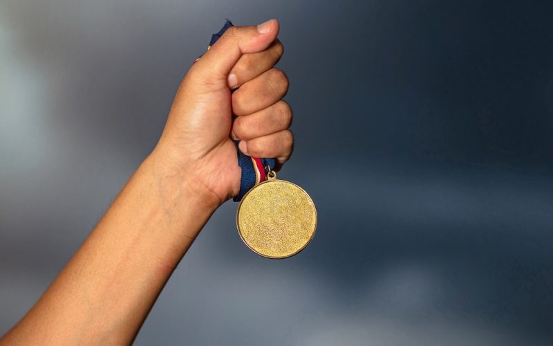 Hand holding gold medal on against cloudy sky background Hand holding gold medal on against cloudy sky background