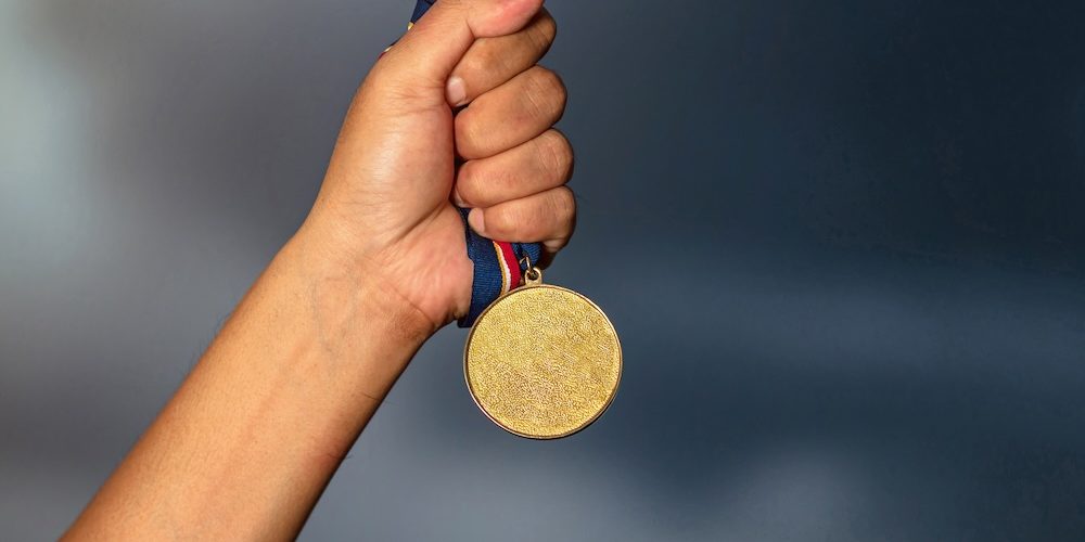 Hand holding gold medal on against cloudy sky background