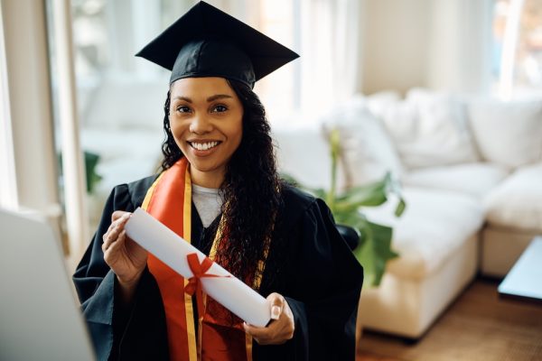 Young black woman in graduation gown holds university certificate and looking at camera. Young black woman in graduation gown holds university certificate and looking at camera.