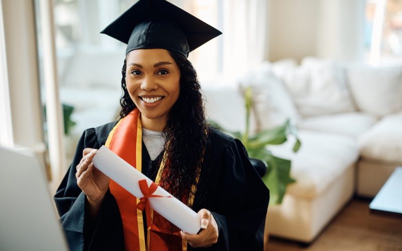 Young black woman in graduation gown holds university certificate and looking at camera. Young black woman in graduation gown holds university certificate and looking at camera.