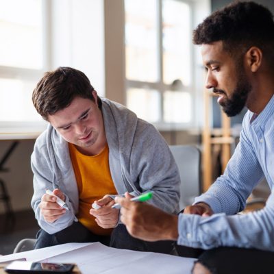 Young man with down syndrome and a caregiver studying indoors