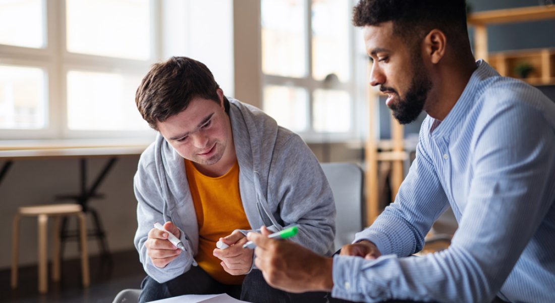 Young man with down syndrome and a caregiver studying indoors