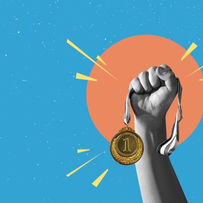 Hand holds and raised gold medal trophy, holding medal against clean background.