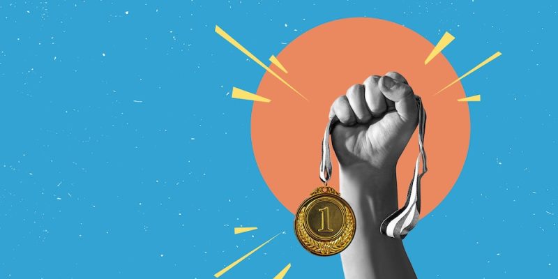 Hand holds and raised gold medal trophy, holding medal against clean background.