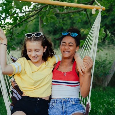 Young teenage girls friends outdoors in garden, swinging on swing.