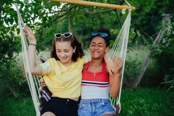 Young teenage girls friends outdoors in garden, swinging on swing.
