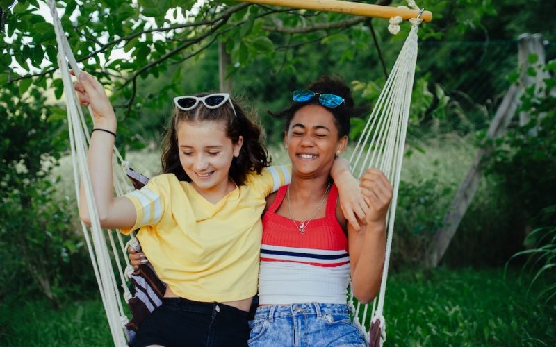 Young teenage girls friends outdoors in garden, swinging on swing.