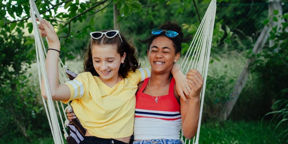 Young teenage girls friends outdoors in garden, swinging on swing.